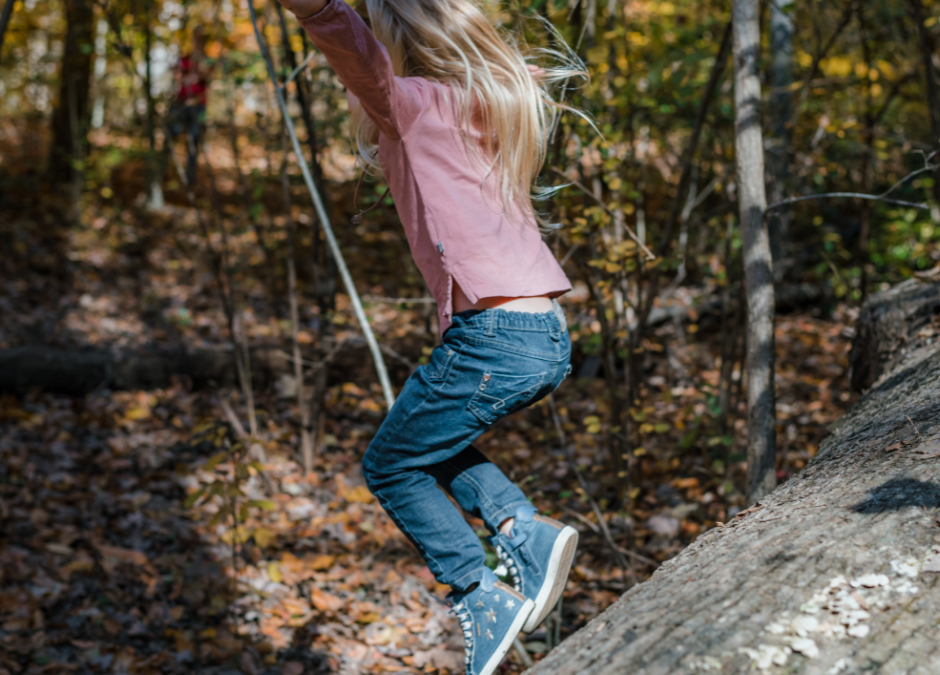 A child jumping off a log onto the soil below